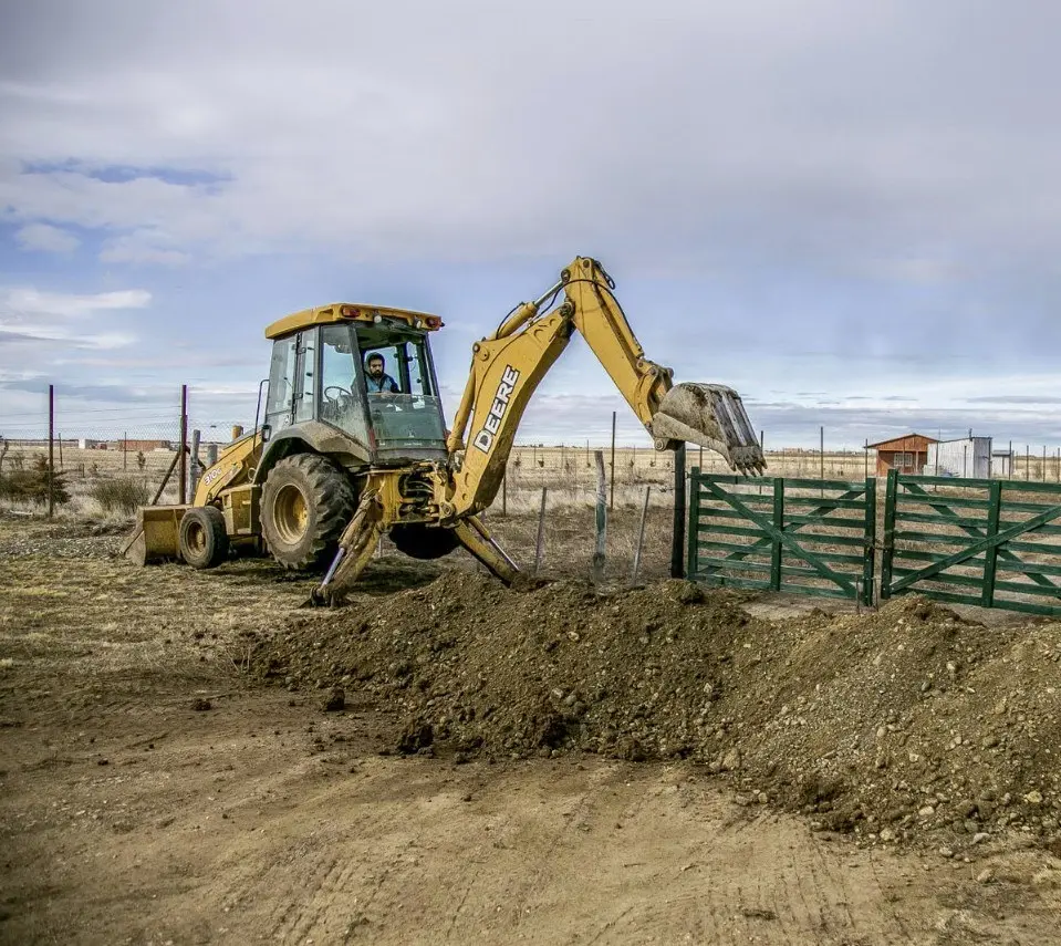Backhoe excavator digging in open soil on a rural property during a septic system installation